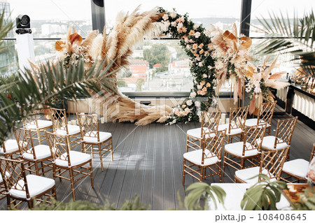 General view of decorated terrace, arch of flowers and chairs stylised in luxury gold tone. Modern decoration concept. General view of decorated terrace, arch of flowers and chairs stylised in luxury gold tone. Modern decoration concept. 108408645