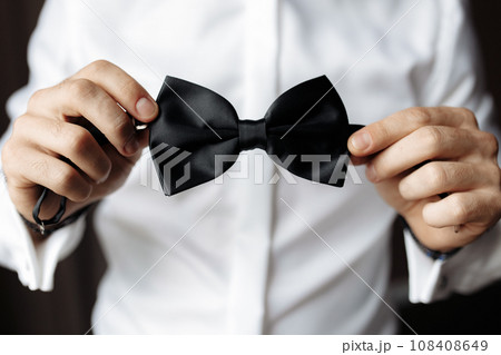 Close up view of man holding black bow tie in hands. Soft focus Close up view of man holding black bow tie in hands. Soft focus 108408649
