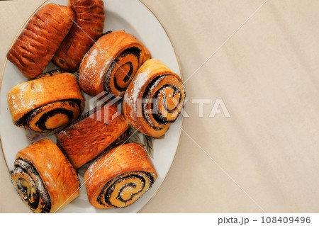 Buns with poppy seeds on a plate on a beige background. Sweet homemade bun. Top view. 108409496