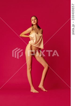 Young beautiful girl posing dressed in underwear and pajama isolated red studio background. Cheerful woman enjoying her morning. 108409857