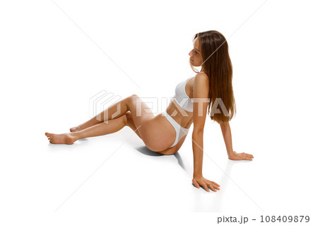 Back view. Young beautiful fit girl with long hair posing in underwear posing sitting on floor isolated white studio background. 108409879