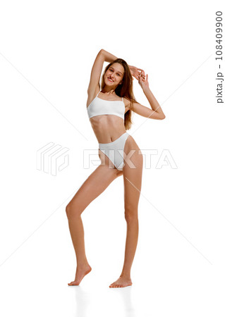 Full length portrait of Slim Caucasian 20s lady posing in white under wear with hands raised up, showing her ideal curves. Full length portrait of Slim Caucasian 20s lady posing in white under wear with hands raised up, showing her ideal curves. 108409900