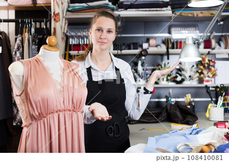 Happy woman tailor in apron standing near mannequin with dress Happy woman tailor in apron standing near mannequin with dress 108410081