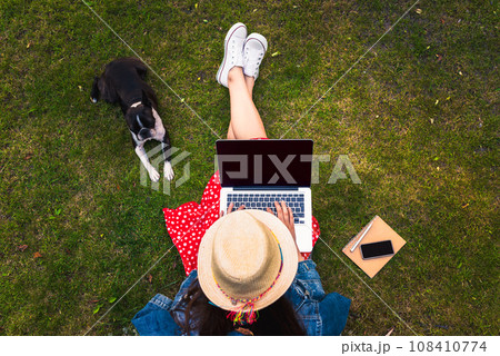 Top view of young woman sitting on grass with her dog and using laptop Top view of young woman sitting on grass with her dog and using laptop 108410774