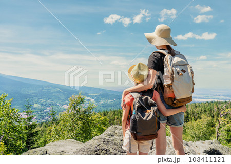 Back view of young two girls with backpacks standing on top of a mountain and looking at the valley 108411121