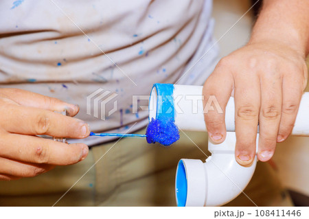 Plumber glues plastic PVC pipes for drainage in new house construction 108411446