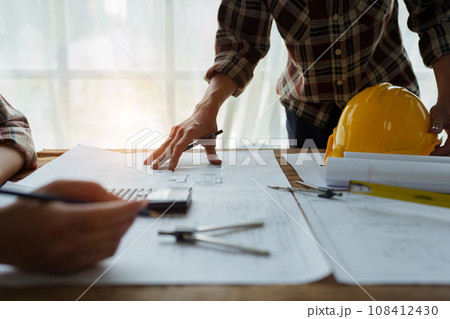 multi ethnic engineer brainstorming and measuring for cost estimating on blueprint and floor plan drawings about design architectural and engineering for houses and buildings. 108412430