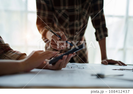 multi ethnic engineer brainstorming and measuring for cost estimating on blueprint and floor plan drawings about design architectural and engineering for houses and buildings. 108412437