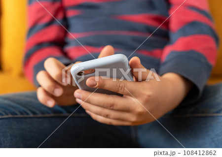 boy is sitting on the couch and using a smartphone boy is sitting on the couch and using a smartphone 108412862