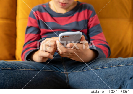 boy is sitting on the couch and using a smartphone 108412864