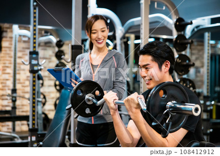 フィットネスジムでトレーナーの指導を受ける男性 108412912