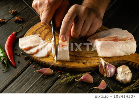 A cook cuts lard on a kitchen board before preparing a delicious garlic appetizer. Peasant food concept 108414307