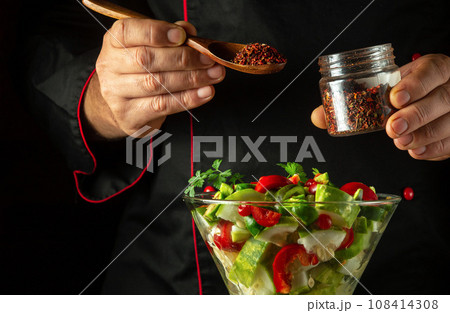 Cooking a healthy salad with the hands of a chef using fresh vegetables for lunch. Adding spices to a bowl of vegetables. Vegetarian food concept in hotel kitchen 108414308