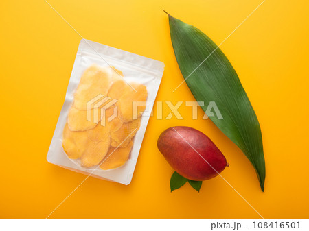 Large pack of dried mango slices with leaf and raw fruit on yellow background.Top view. 108416501
