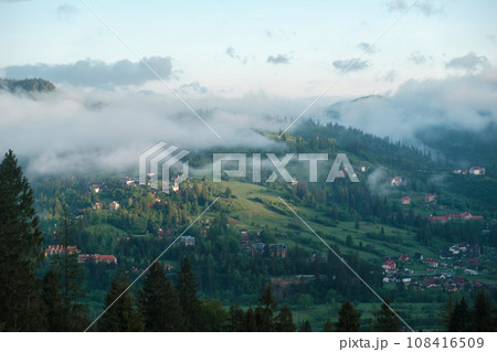 mountainous rural landscape at sunset. beautiful scenery with forests, hills and meadows in evening light. ridge with high peak in the distance. village in the distant valley 108416509