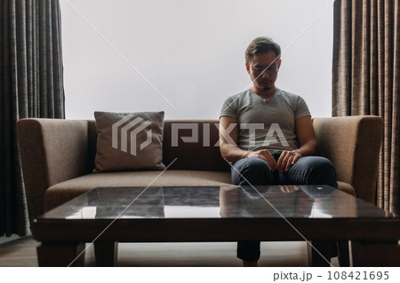 Lonely man sits on the sofa thinking of his lover. 108421695