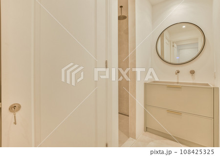 a bathroom with a mirror on the wall and white cupboards in front of the bathtub is next to the door 108425325
