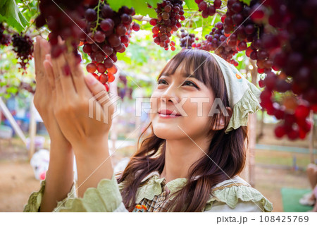 Woman in cute dress holding grapes in a vineyard Woman in cute dress holding grapes in a vineyard 108425769