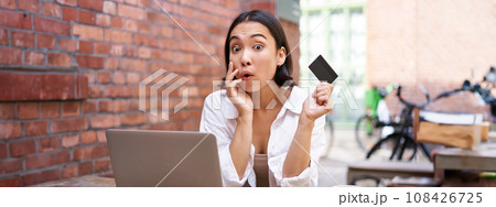 Stylish young asian woman doing shopping online, sitting with credit card and laptop, buying in internet and paying contactless, dealing with bills Stylish young asian woman doing shopping online, sitting with credit card and laptop, buying in internet and paying contactless, dealing with bills 108426725