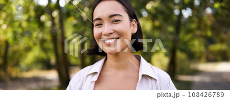 People concept. Smiling asian girl looking at camera with happy, joyful emotion, posing in green park on a warm summer day 108426789