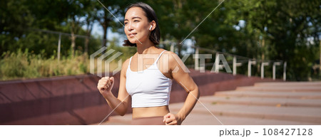 Wellbeing and sport. Asian fitness girl runner, jogging in park, running on street in leggings, smiling happily 108427128