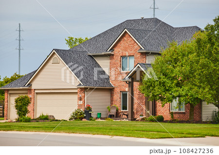 Suburban home with reddish brown brick face and overhang over front door side view 108427236