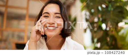 Close up portrait of funny young asian woman, sitting in cafe, chatting lively, smiling at camera 108427240