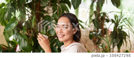 Vertical shot of young asian woman with digital tablet and graphic pen, drawing, scratching while sitting in cafe with cup of coffee Vertical shot of young asian woman with digital tablet and graphic pen, drawing, scratching while sitting in cafe with cup of coffee 108427298