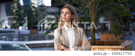 Close up portrait of confident and successful businesswoman in suit, cross arms on chest, standing in power pose on street near office building 108427750