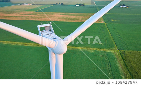 Close up of sunrise golden hour lighting on wind turbine blades in lush green field aerial Close up of sunrise golden hour lighting on wind turbine blades in lush green field aerial 108427947
