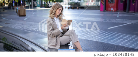 Woman working, writing down thoughts in her planner, sitting in city centre in business clothing 108428148