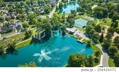 Aerial over Lakeside Pond with fountain near playground and tennis courts in neighborhood 108428371