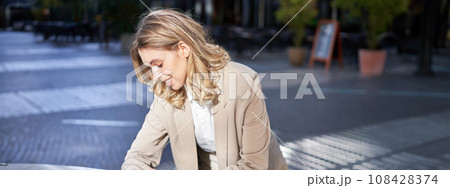 Portrait of businesswoman looks at her digital watch to check time, standing outside on street near office 108428374
