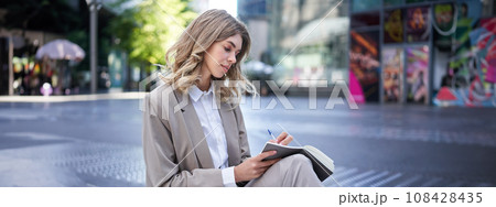 Woman working, writing down thoughts in her planner, sitting in city centre in business clothing 108428435