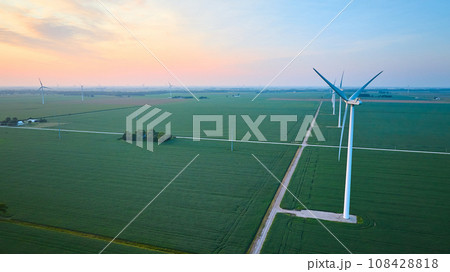 Aerial row of wind turbines in green farmland fields at sunrise or sunset with orange and pink sky 108428818