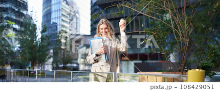 Enthusiastic businesswoman feels upbeat after morning cup of coffee, raise her cup up and dances outside Enthusiastic businesswoman feels upbeat after morning cup of coffee, raise her cup up and dances outside 108429051