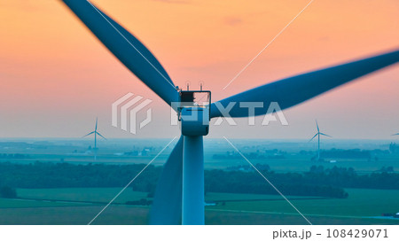 Aerial straight of back of wind turbine with distant turbines in green farmland at sunset Aerial straight of back of wind turbine with distant turbines in green farmland at sunset 108429071