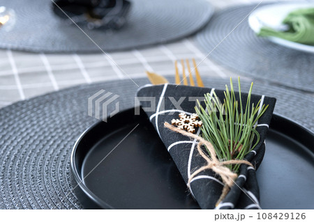 Serving a festive table with plates, forks, knives, napkins close-up tissue in a cage decorated for Christmas and New Year pine branch with a cone. Eco-style, minimalism 108429126