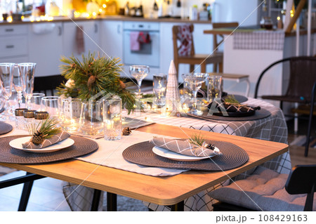 Serving a festive table with plates, forks, knives, napkins, glasses close-up in the modern interior of a loft house decorated for Christmas and New Year. Waiting for guests for a festive dinner Serving a festive table with plates, forks, knives, napkins, glasses close-up in the modern interior of a loft house decorated for Christmas and New Year. Waiting for guests for a festive dinner 108429163