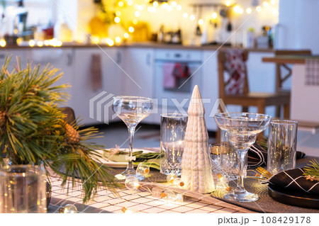 Serving a festive table with plates, forks, knives, napkins, glasses close-up in the modern interior of a loft house decorated for Christmas and New Year. Waiting for guests for a festive dinner Serving a festive table with plates, forks, knives, napkins, glasses close-up in the modern interior of a loft house decorated for Christmas and New Year. Waiting for guests for a festive dinner 108429178