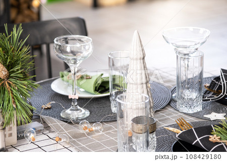 Serving a festive table with plates, forks, knives, napkins, glasses close-up in the modern interior of a loft house decorated for Christmas and New Year. Waiting for guests for a festive dinner Serving a festive table with plates, forks, knives, napkins, glasses close-up in the modern interior of a loft house decorated for Christmas and New Year. Waiting for guests for a festive dinner 108429180