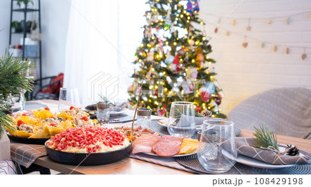 Serving a festive table with snacks, salads and goodies close-up in the modern interior of a loft house decorated for Christmas and New Year. Waiting for guests for a festive dinner Serving a festive table with snacks, salads and goodies close-up in the modern interior of a loft house decorated for Christmas and New Year. Waiting for guests for a festive dinner 108429198