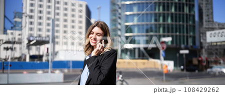 Beautiful female manager, ceo of company, walking on street, smiling and talking on mobile phone on sunny day 108429262