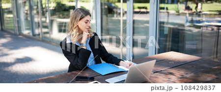 Successful businesswoman working outdoors. Corporate woman sitting on bench with laptop, writing, taking notes during work meeting Successful businesswoman working outdoors. Corporate woman sitting on bench with laptop, writing, taking notes during work meeting 108429837