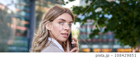 Close up shot of businesswoman talking on mobile phone. Corporate woman calling someone, looking around, standing outdoors 108429851