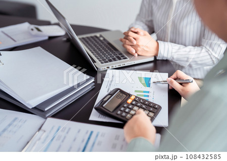 Two business real estate seller using calculator to calculating about property investment and pointing on document to explaining terms data about home sales contract and home insurance in office Two business real estate seller using calculator to calculating about property investment and pointing on document to explaining terms data about home sales contract and home insurance in office 108432585