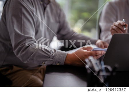 Two businessman real estate sellers are read property investment document to checking finance data on laptop while discussion and brainstorming about home sales contract and home insurance in office 108432587