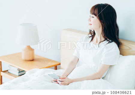 ベッドでスマートフォンを使う女性。 ベッドでスマートフォンを使う女性。 108436621