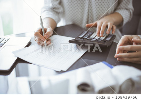 Woman accountant using a calculator and laptop computer while counting taxes for a client. Business audit concepts 108439766