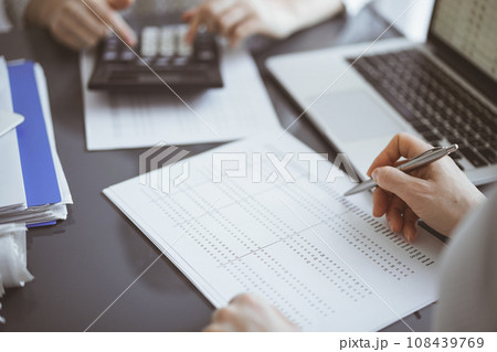 Woman accountant using a calculator and laptop computer while counting taxes for a client. Business audit concepts 108439769